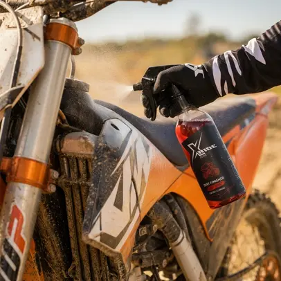 A user applying Xzone Dirt Finisher professional preparation to a dirty off-road motorcycle for cleaning and protection.