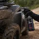 A user spraying a muddy quad wheel arch with Xzone Mud Breaker professional cleaner.